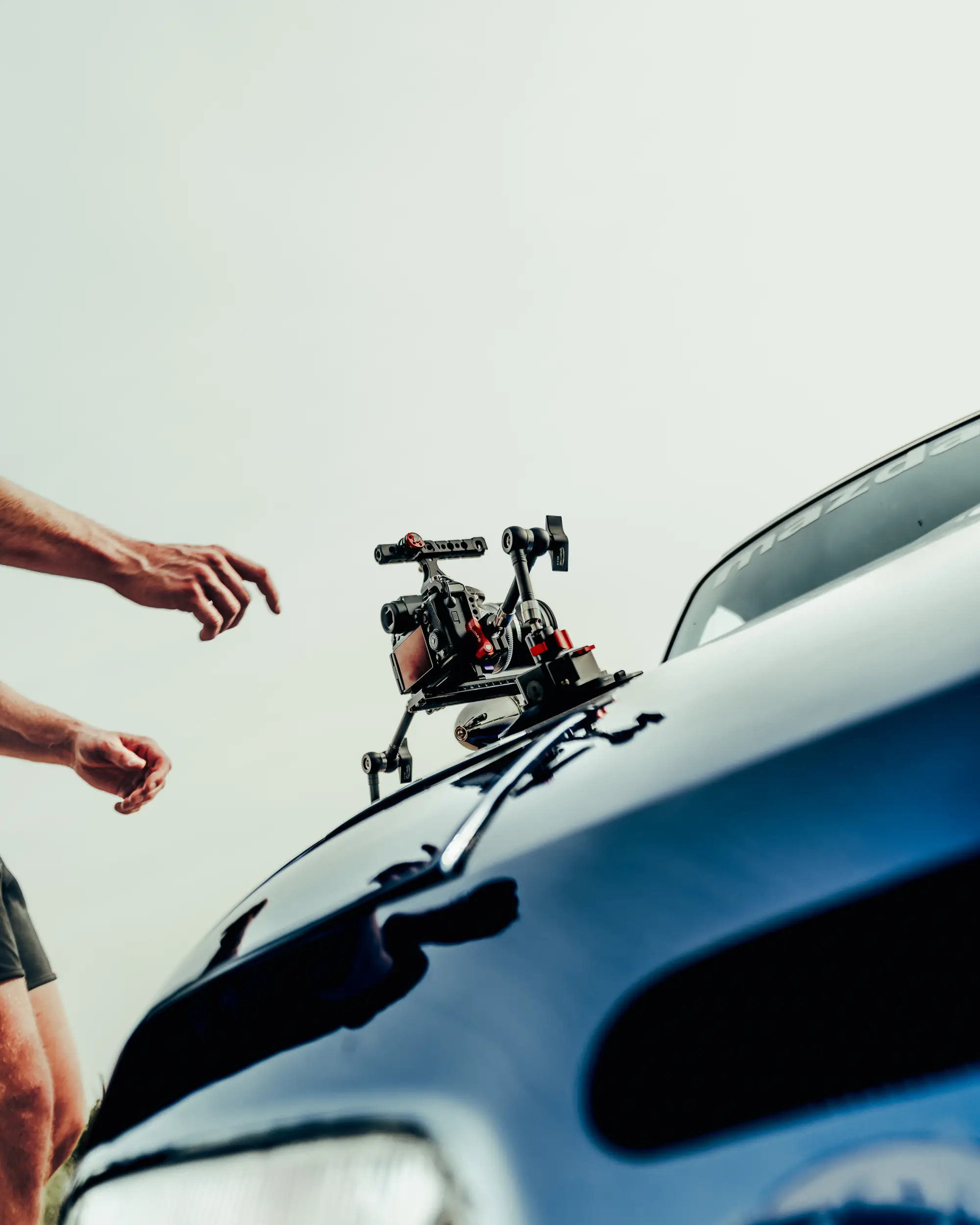 Kamera mit Saugnapfhalterung auf der Motorhaube eines dunkelblauen Mazda MX-5, Hände greifen von links ins Bild